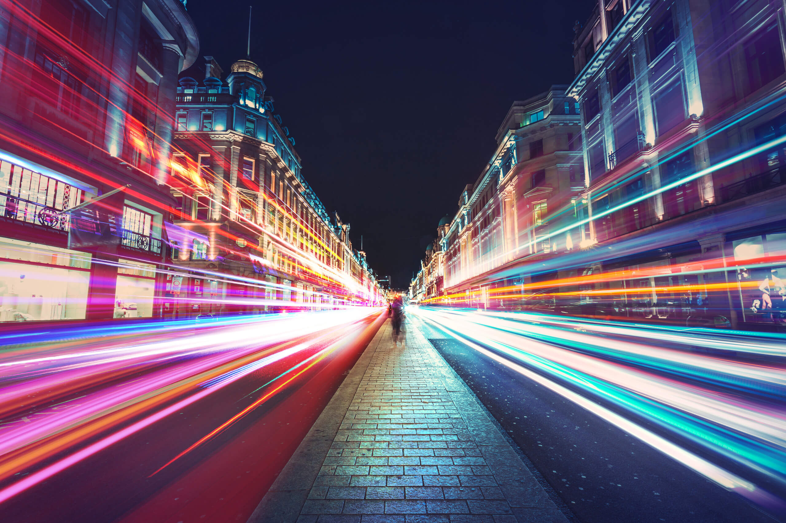 Blurred people standing in a meridian on a busy street of London, motion speed lights are streaming on both sides of them.